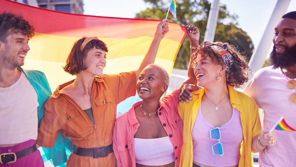 Company of friends of different sizes, ages and genders together under rainbow flags.