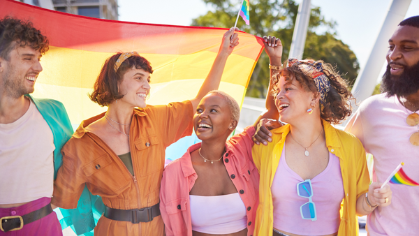 Group of diverse people lit by the light filtering through a rainbow flag.