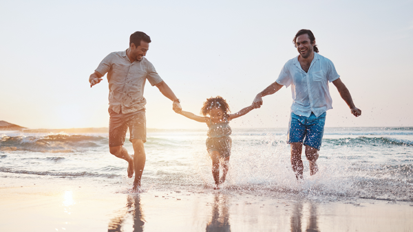 Little splushing in water at seaside with her same-sex parents