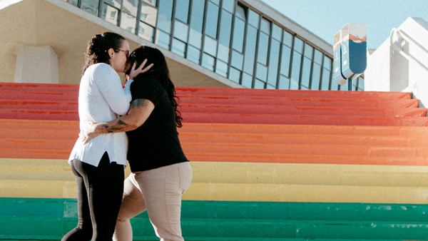 Same-sex couple kissing on a public rainbow-coloured staircase 