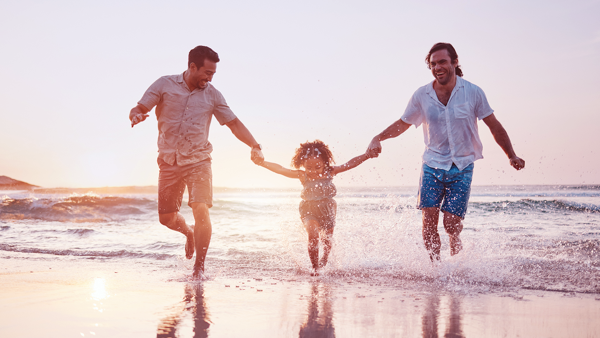 Little girl running by the sea with two fathers.